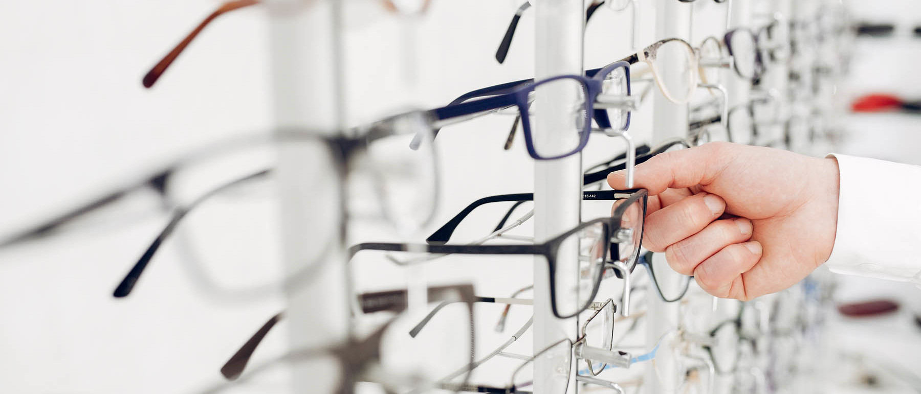 A person is selecting eyeglasses from a rack in an eye care store.