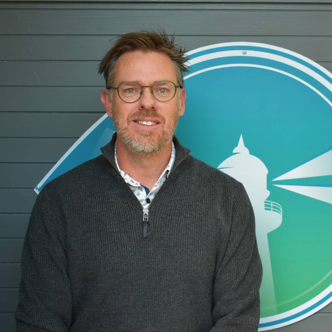 A man named Steven standing in front of a lighthouse logo.