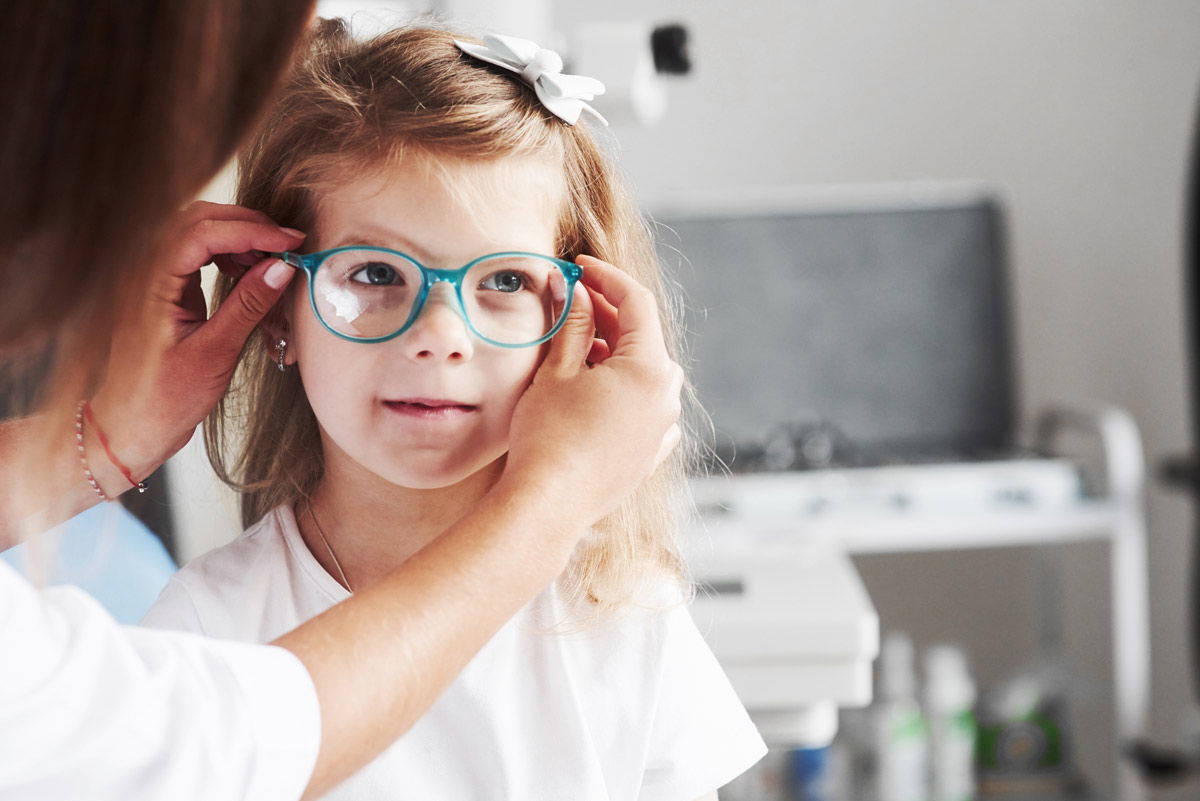 A young girl is getting her eyeglasses adjusted by an optometrist.