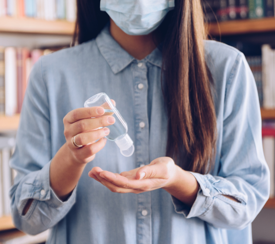 A woman wearing a surgical mask holding a bottle of disinfectant.