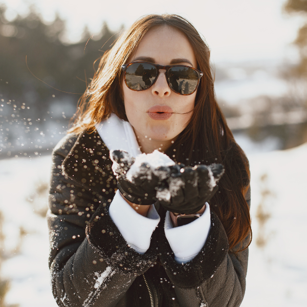 A woman in sunglasses blowing snow into the air.