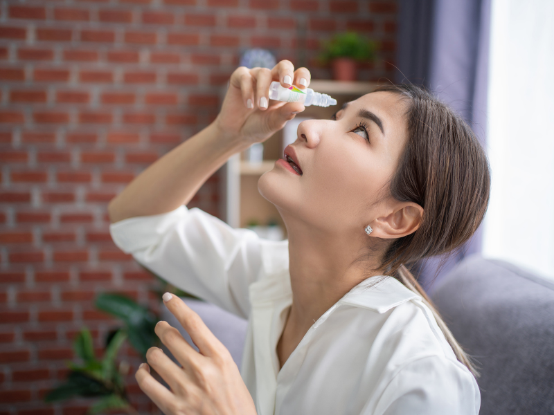 A woman is using a nasal spray at home.