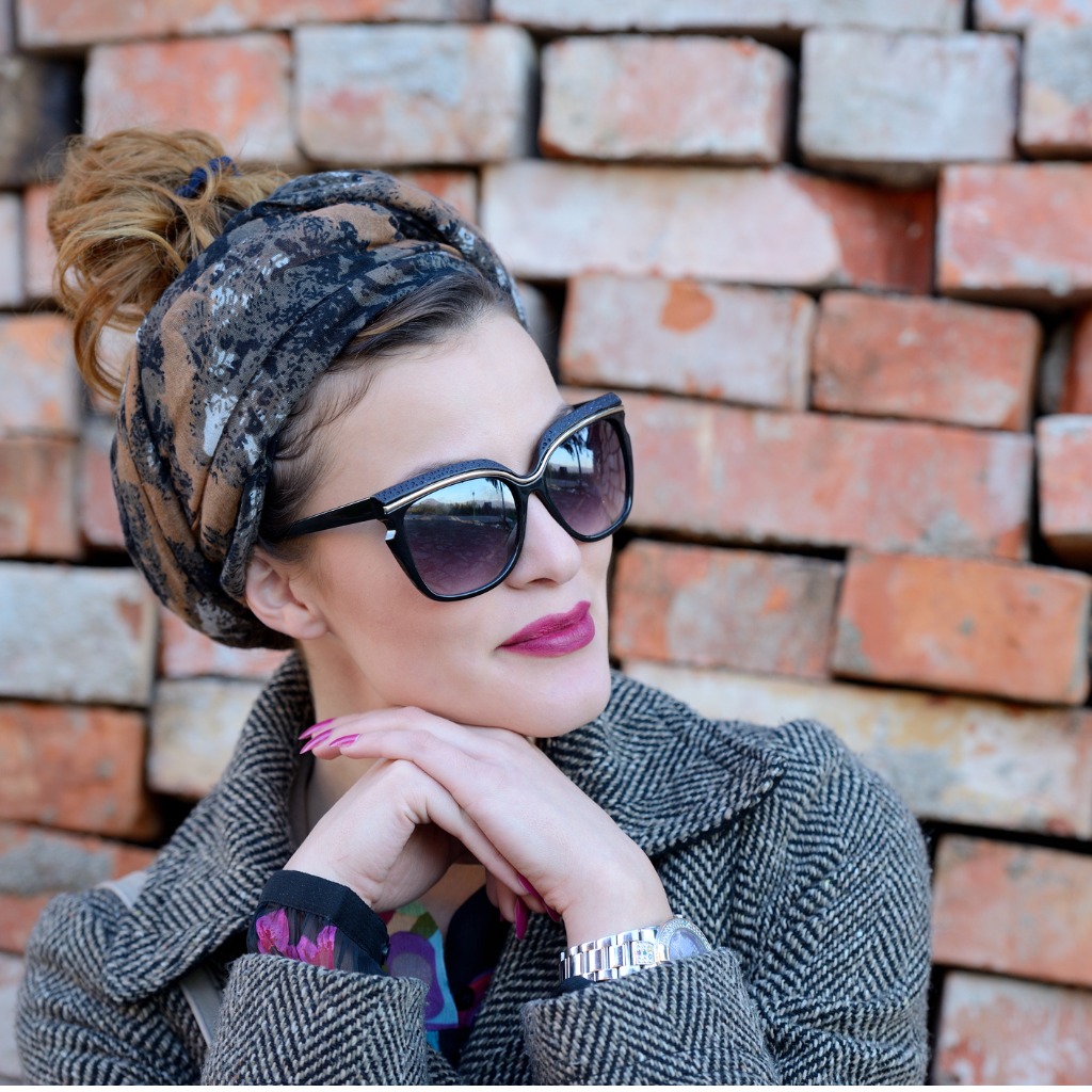A woman wearing sunglasses leaning against a brick wall.