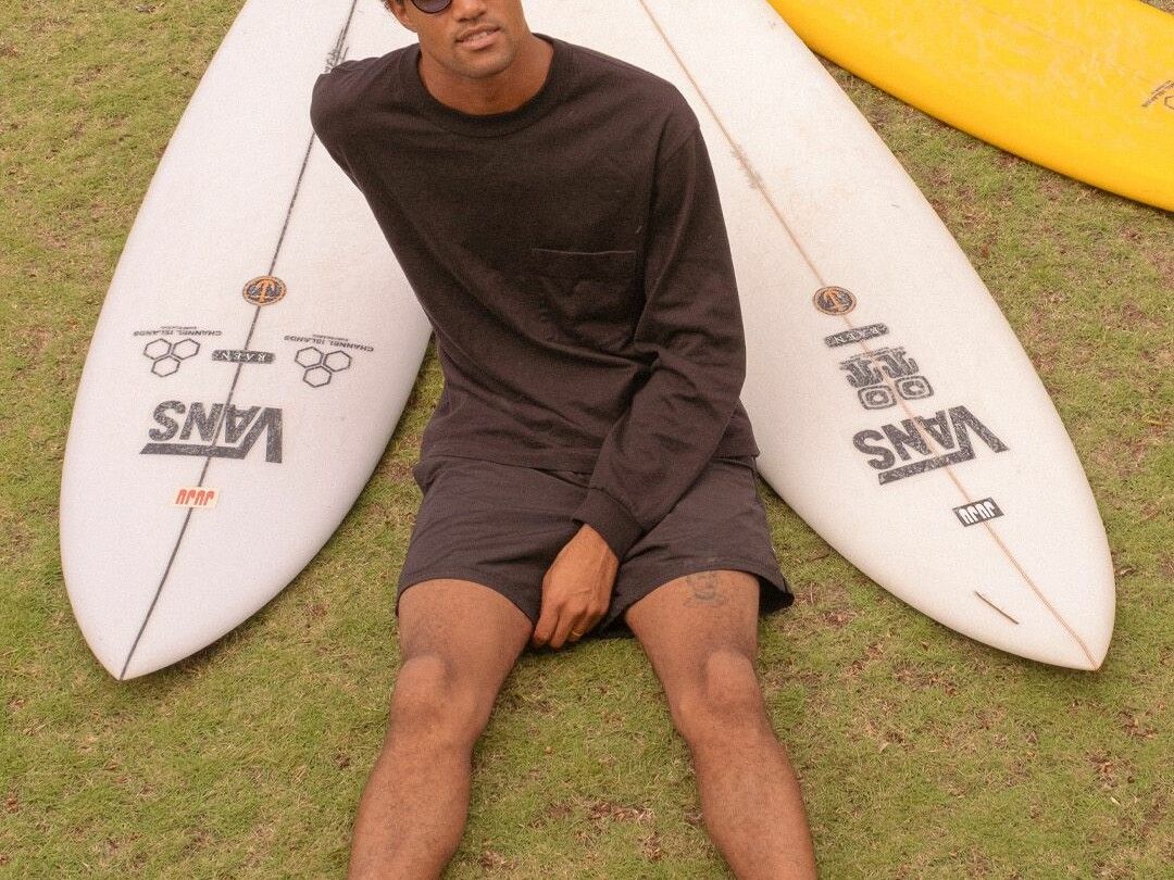 A person sitting on the grass with surfboards propped up behind them.