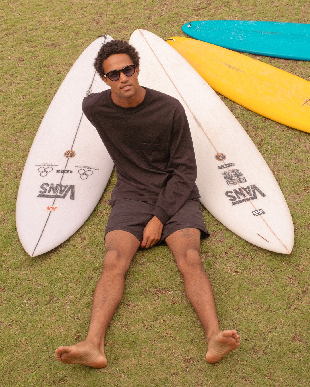 A person sitting on the grass with surfboards propped up behind them.