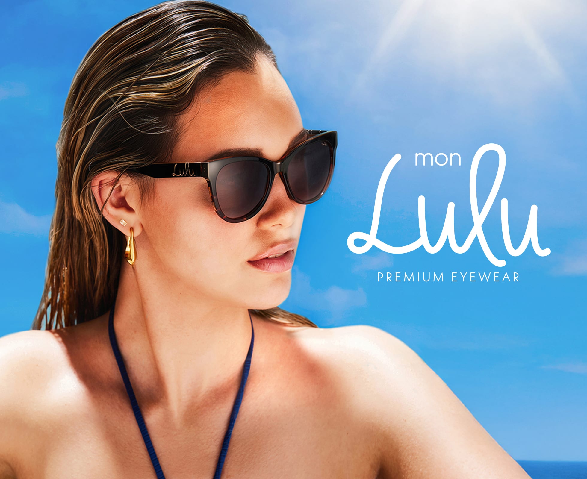 A woman wearing black sunglasses and gold earrings poses against a blue sky with 