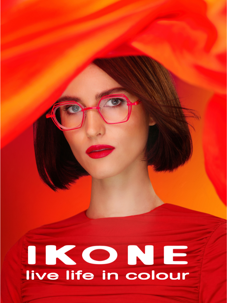 Woman with short brown hair and red glasses, wearing a red top, stands against an orange background. Text reads "IKONE live life in colour.